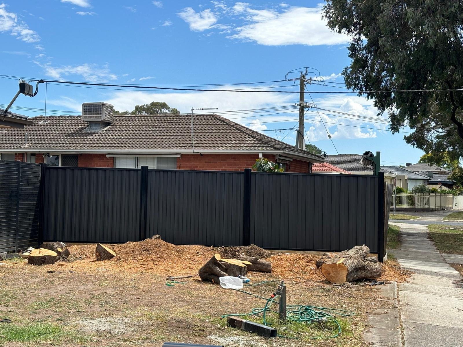 Cleared backyard with tree stumps and a black Colorbond fence, ready for retaining wall and levelling work in Melbourne